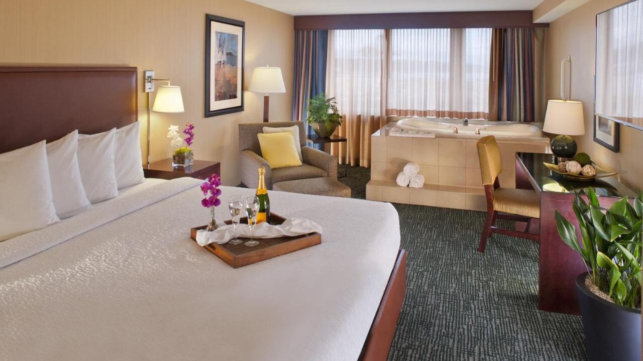 Hotel suite bedroom with in-room Jacuzzi tub, large windows, seating area, and romantic amenities